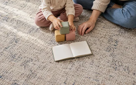 A child playing with soft blocks beside a parent's hand.